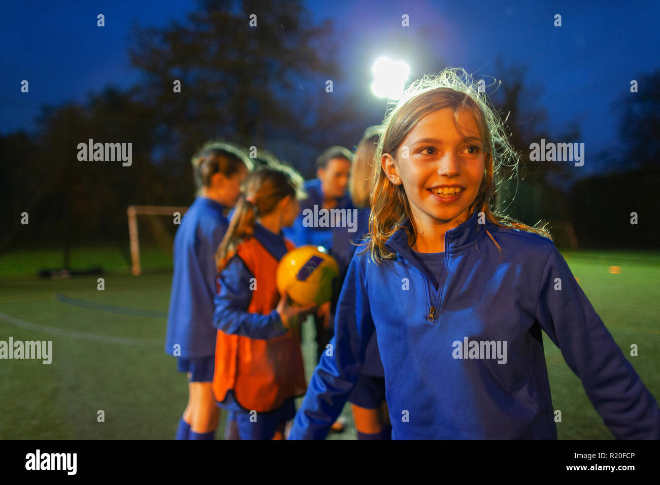Ragazza sorridente che giocano a calcio sul campo di notte Foto Stock
