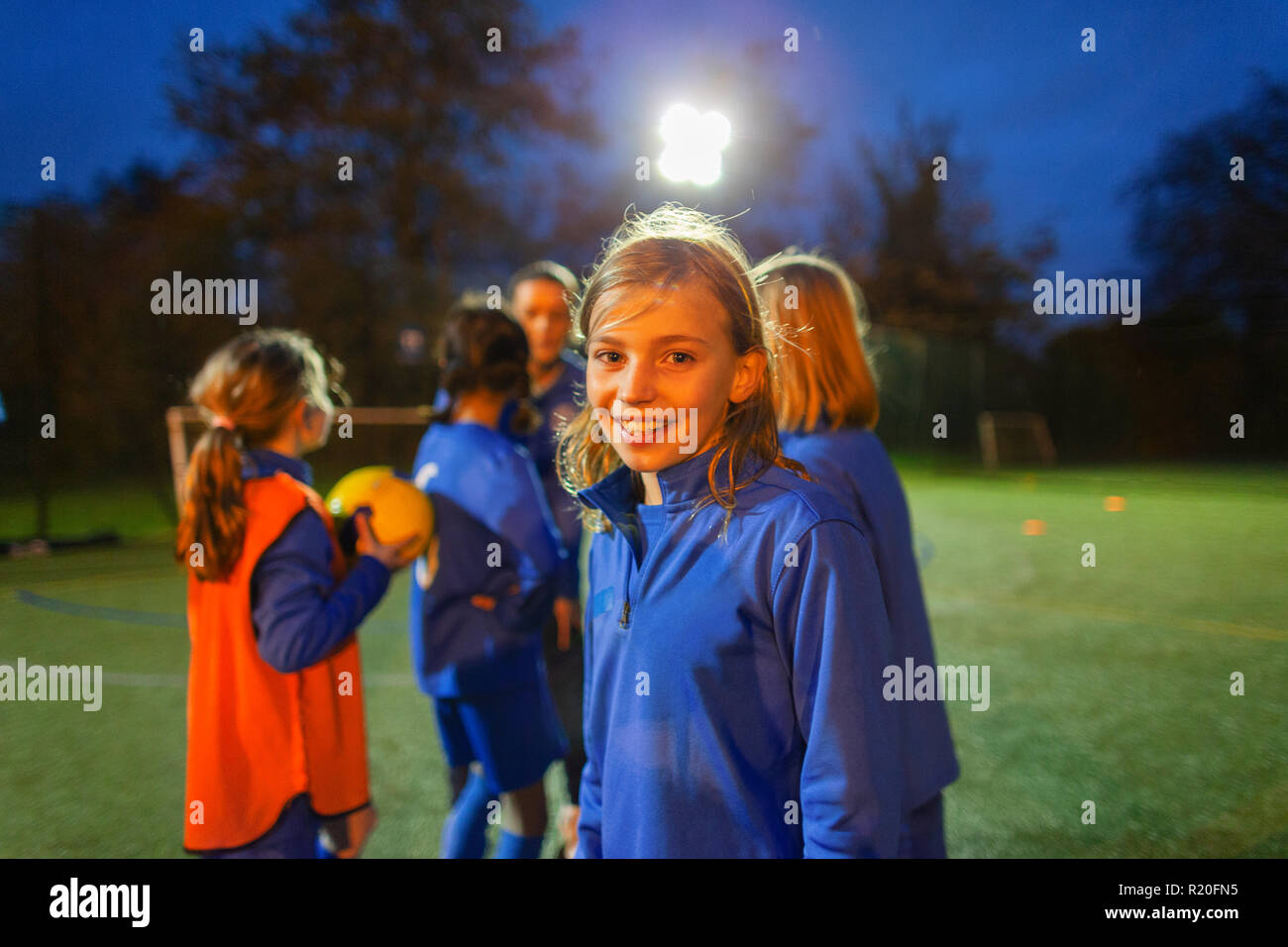 Ritratto sorridente ragazza fiducioso giocatore di calcio sul campo di notte Foto Stock