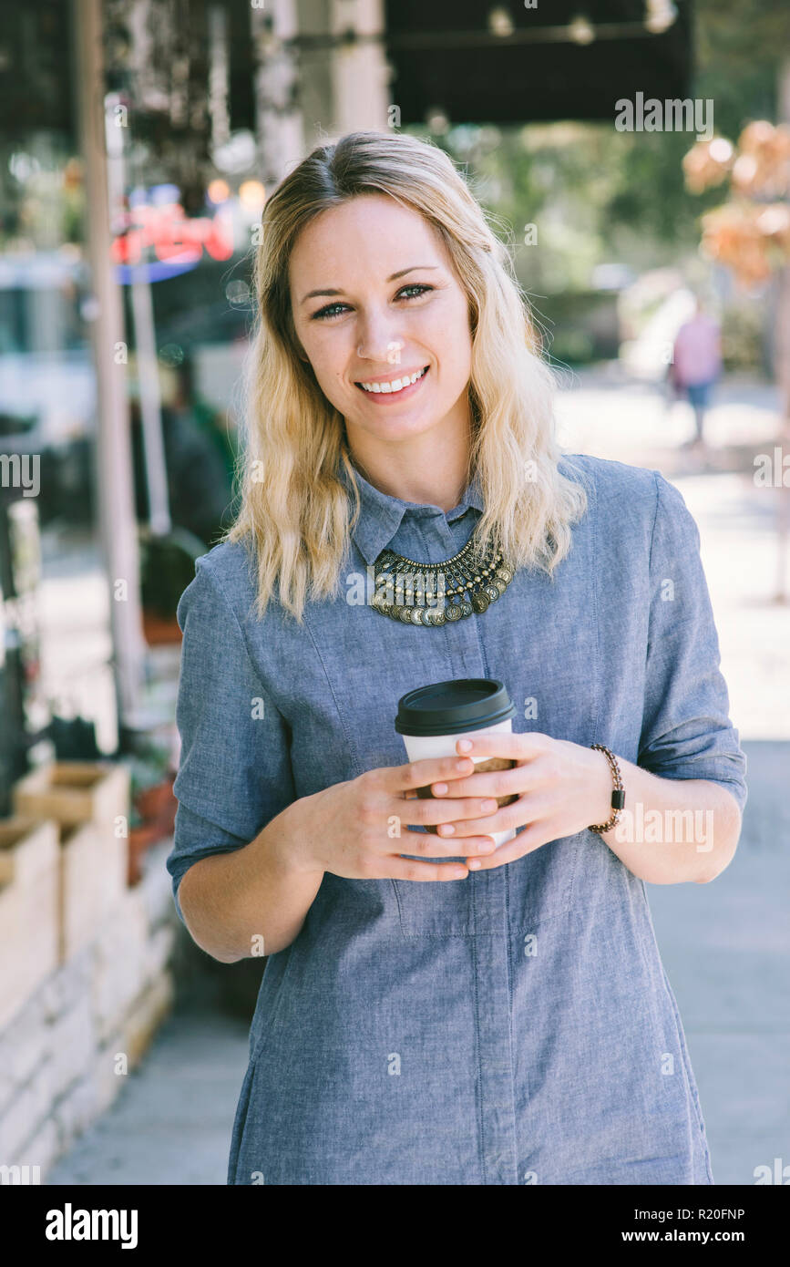 Una bionda femmina caucasica beve caffè mentre sorridente Foto Stock