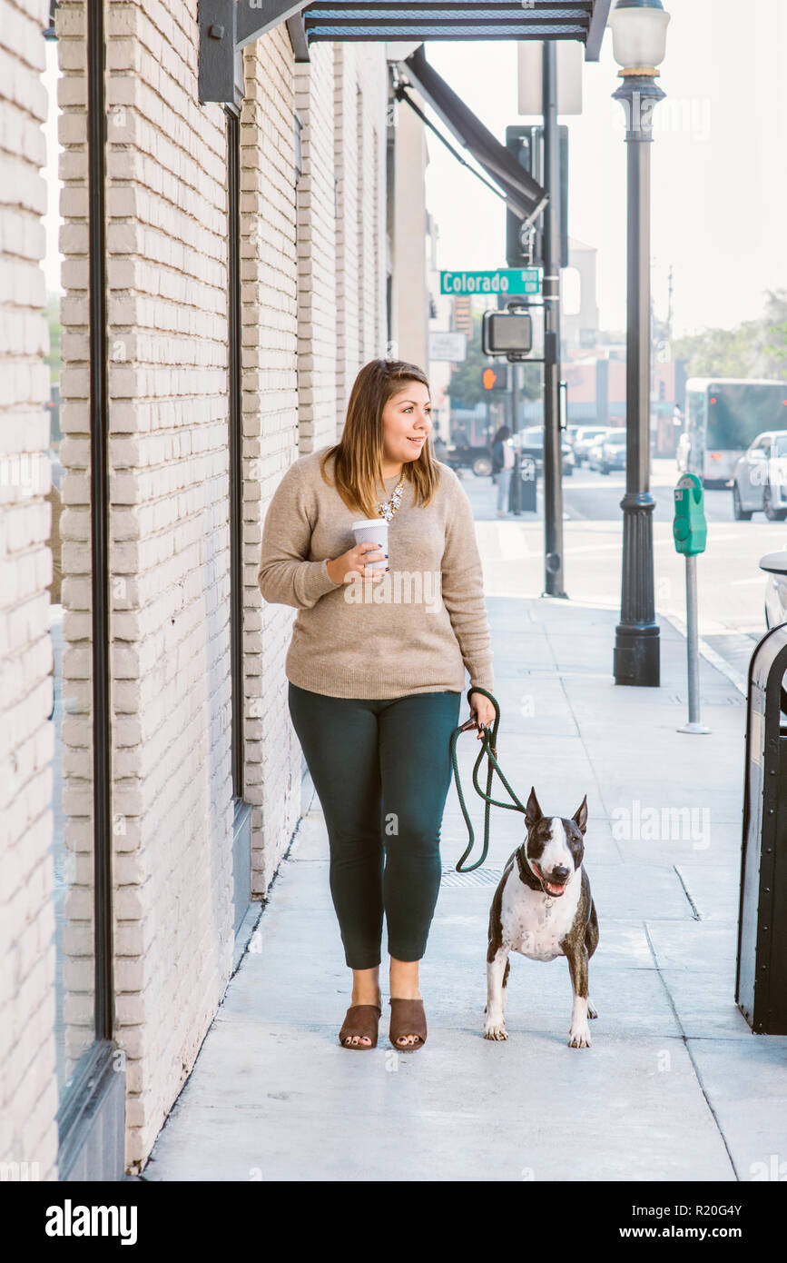 Una femmina di Latina cammina il suo cane mentre si sorseggia un caffè nella città Foto Stock