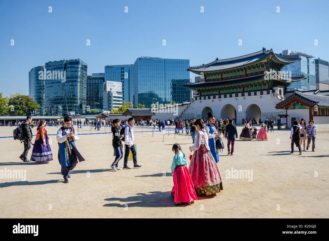 La giustapposizione di vecchio palazzo Gyeongbokgung insieme contro l'architettura moderna. Il cortile è pieno di turisti indossando il tradizionale abito coreano. Foto Stock