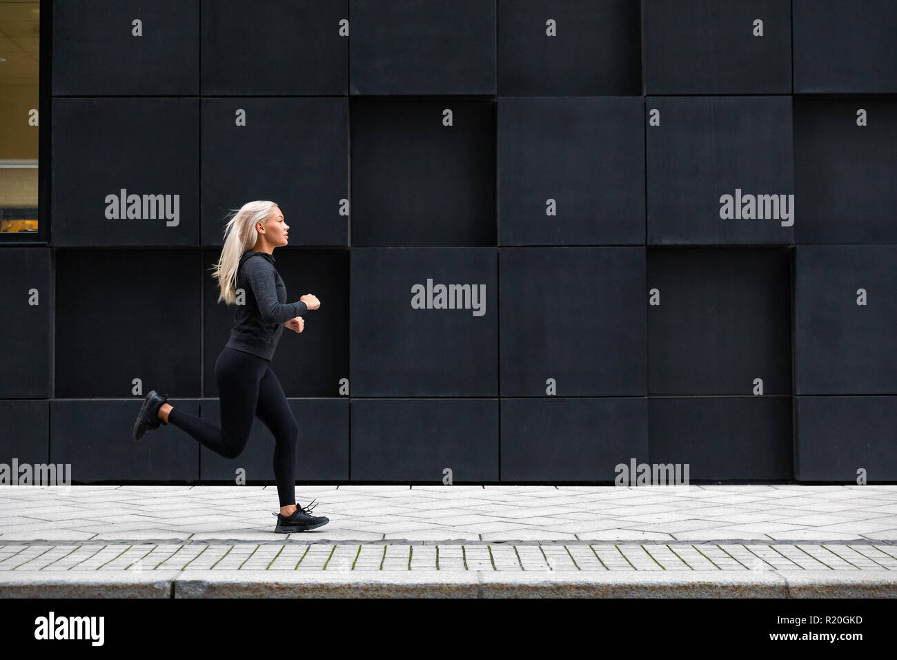 La donna in esecuzione sulla strada di città contro città moderna di pareti Foto Stock