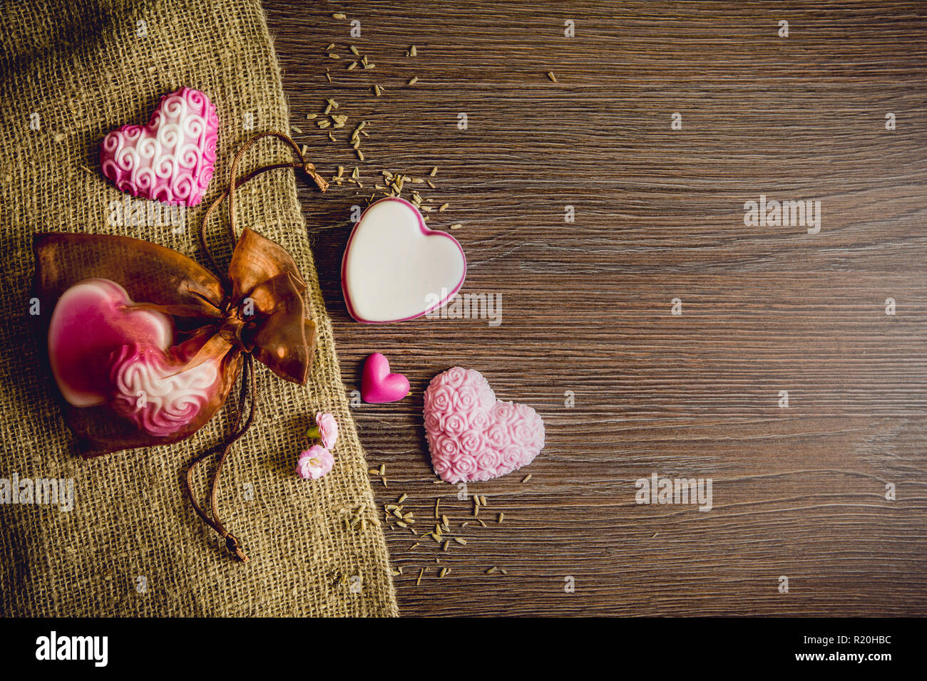 I diversi colori fatto a mano forma di cuore saponi sulla tavola di legno sfondo, tela ruvida stoffa e in tulle marrone borsa regalo. Fatto a mano idea regalo concetto. Sacco di co Foto Stock