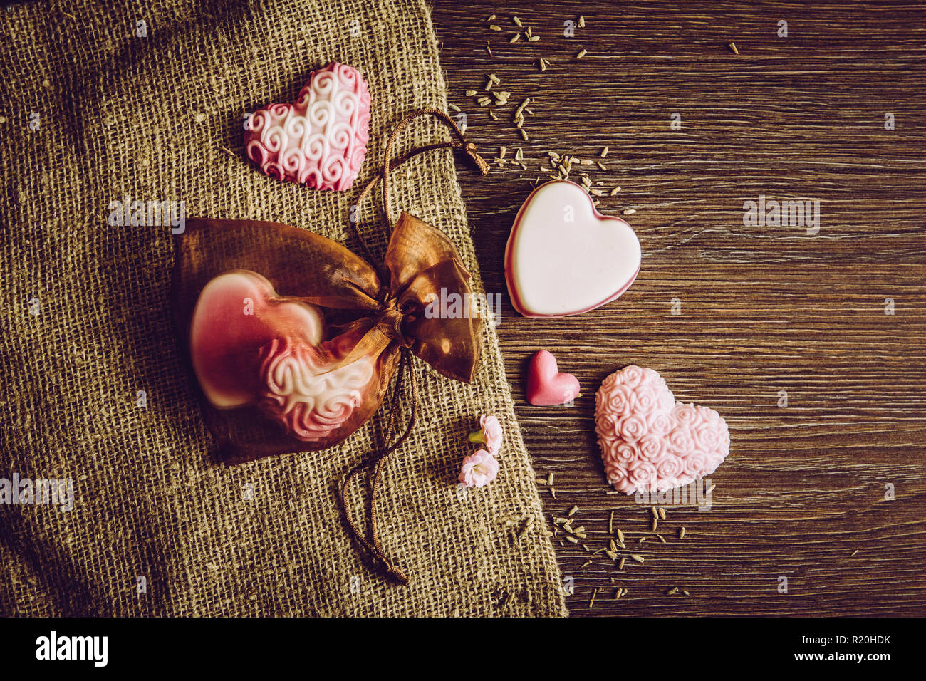 I diversi colori fatto a mano forma di cuore saponi sulla tavola di legno sfondo, tela ruvida stoffa e in tulle marrone borsa regalo. Fatto a mano idea regalo concetto. Sacco di co Foto Stock