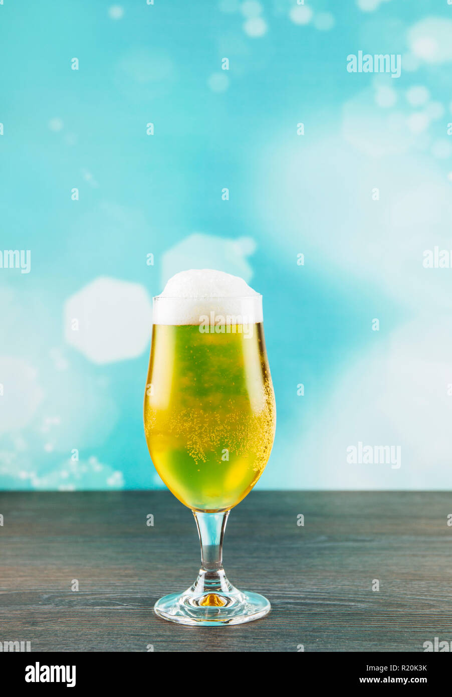 Calice birra stile vetro su naturale scuro tavolo in legno con luce blu sfondo bokeh di fondo. Foto Stock