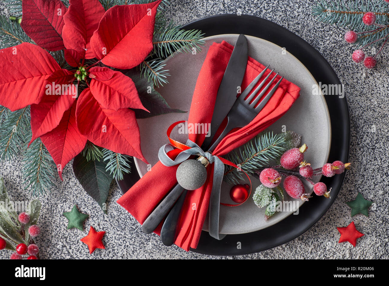 Tavola di Natale impostazione sul granito grigio, nero e grigio piatti, tovagliolo rosso decorato con poinsettia e bacche smerigliato Foto Stock