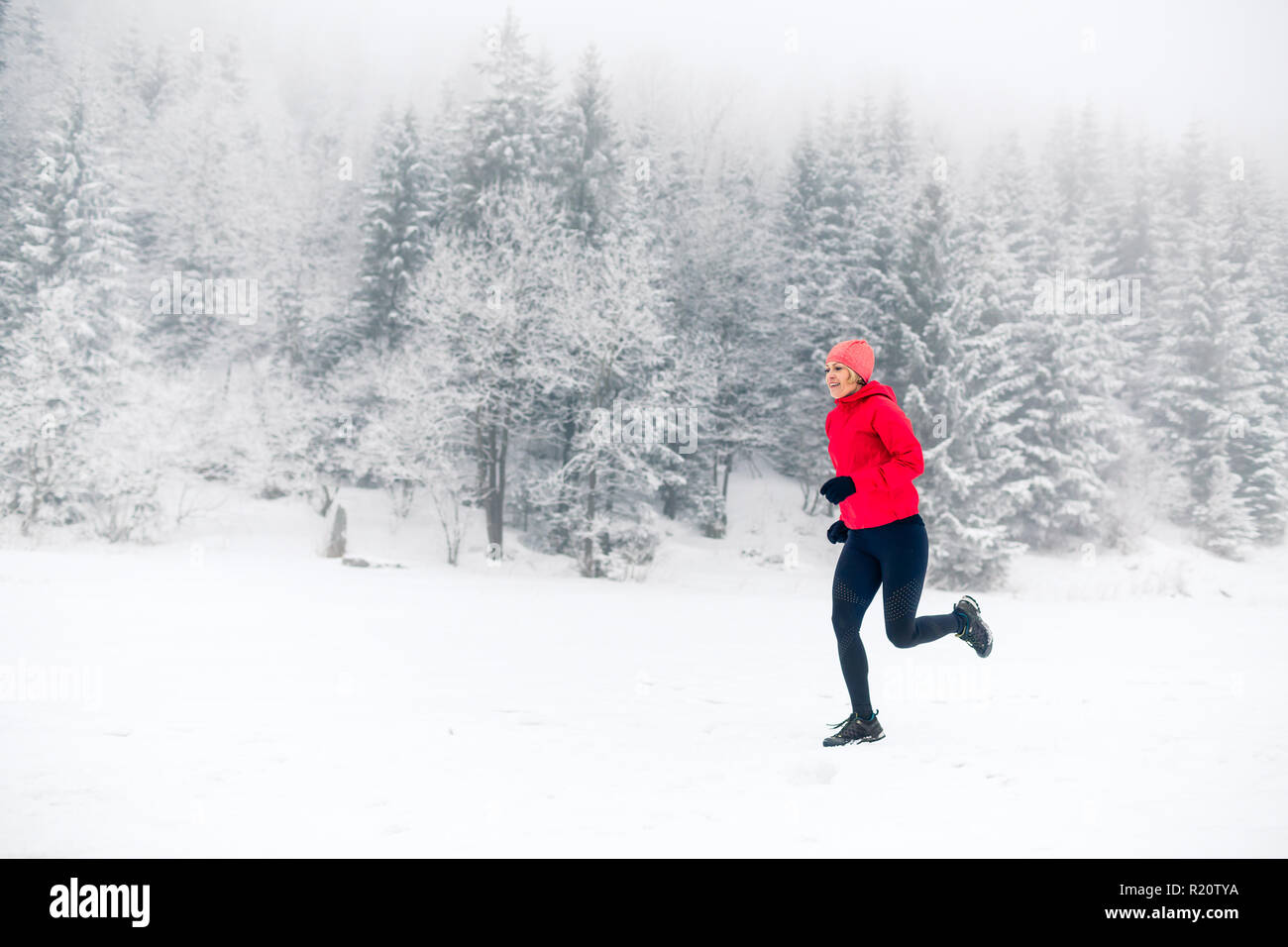 Ragazza che corre sulla neve in inverno le montagne. Sport e fitness ispirazione e motivazione. Giovane donna felice trail running in montagna sulla neve, giorno d'inverno. Foto Stock