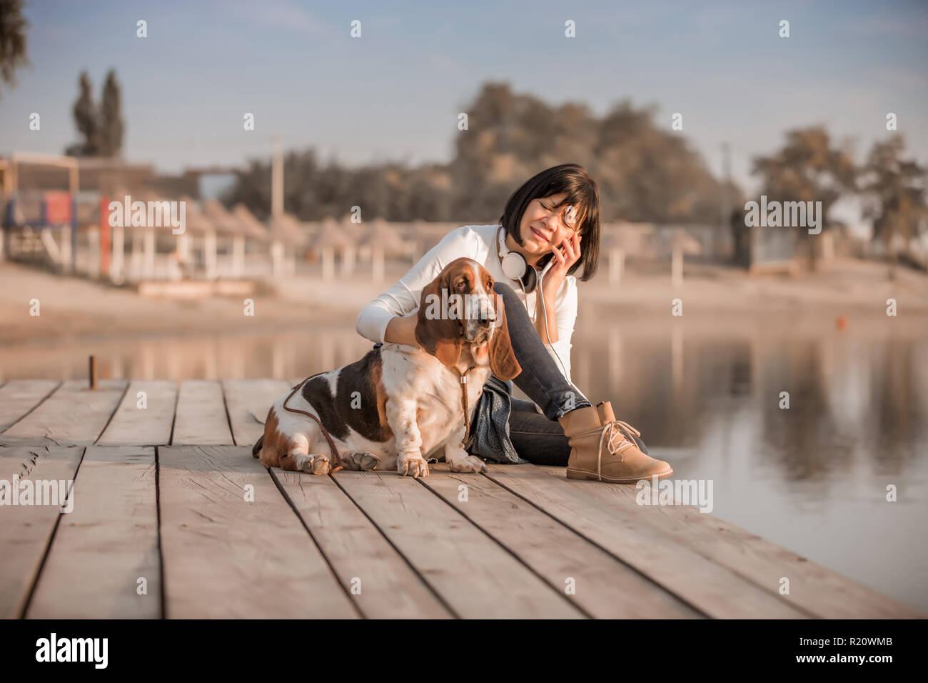 Ritratto di giovane e bella donna seduta presso il fiume con il suo cane Basset Hound mentre parlano al telefono cellulare Foto Stock