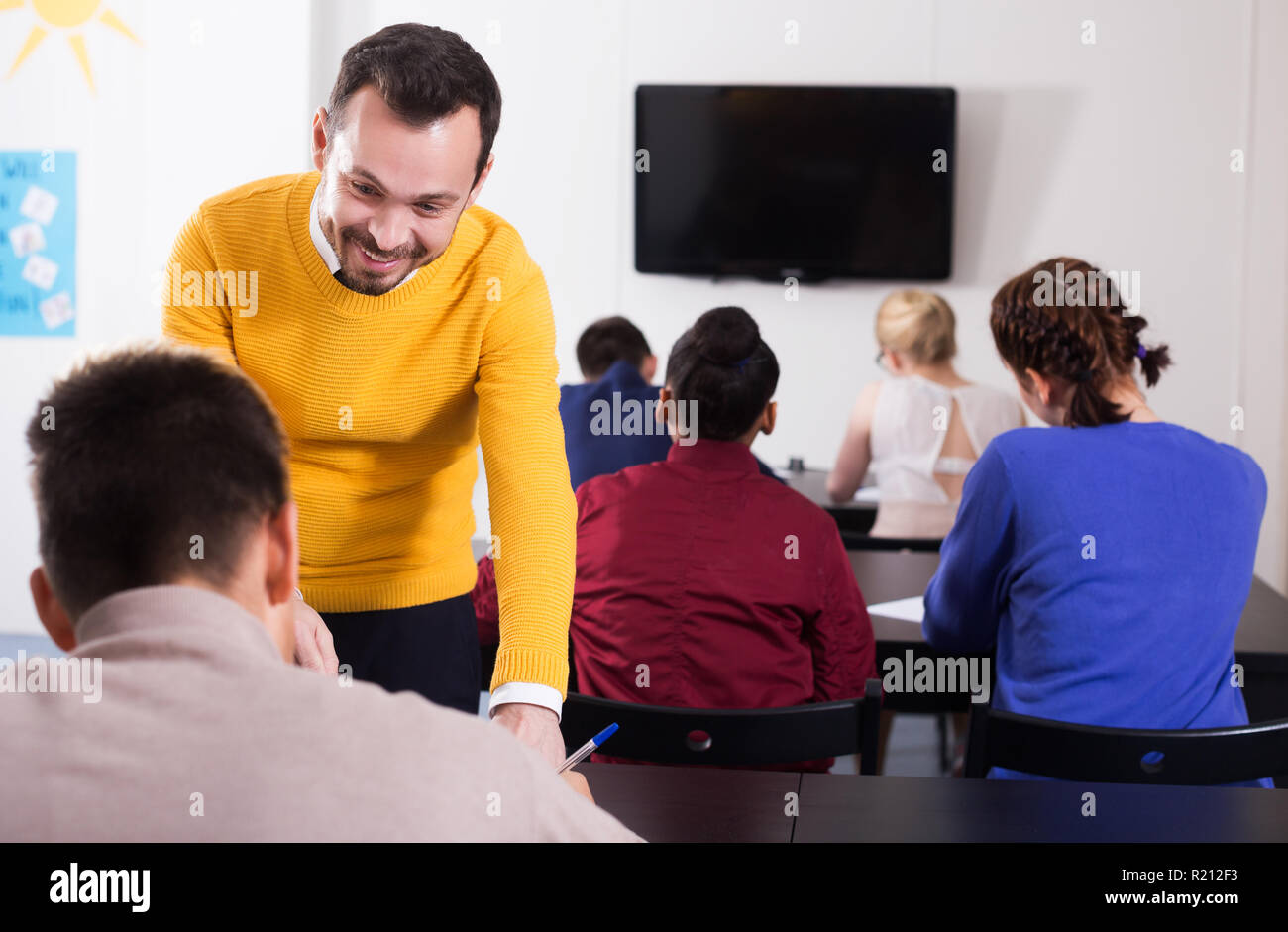 Felice giovane insegnante dare spiegazione agli studenti durante il lavoro di revisione in classe Foto Stock