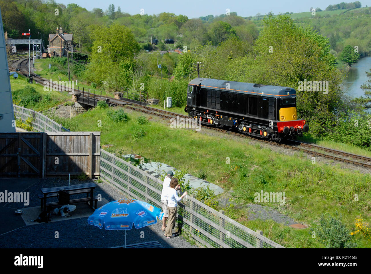 Due persone che guardano la locomotiva diesel passano sul tratto di single-via linea ferroviaria, Inghilterra Foto Stock