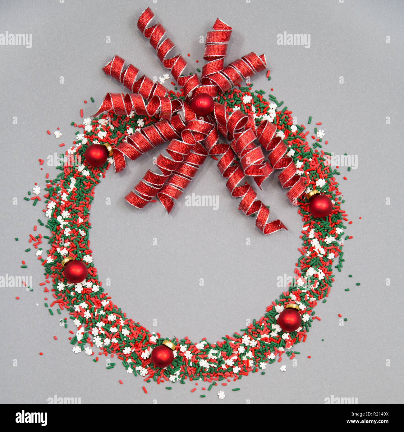 Ghirlanda di Natale fatto di rosso e verde irrora con ornamenti natale e un archetto a spirale su sfondo grigio Foto Stock