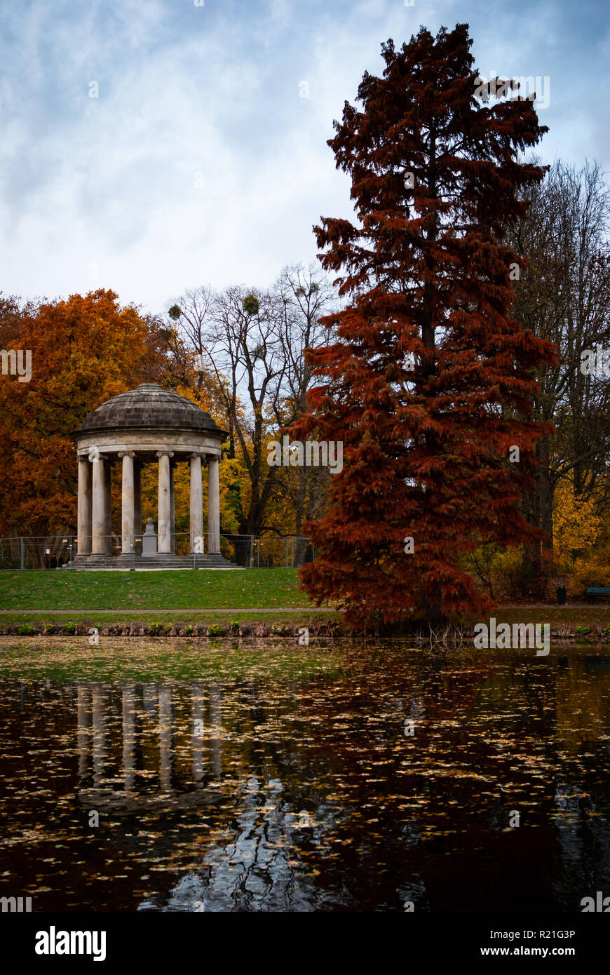 Un padiglione in pietra su un prato verde circondato da grandi alberi con foglie colorate in autunno Foto Stock
