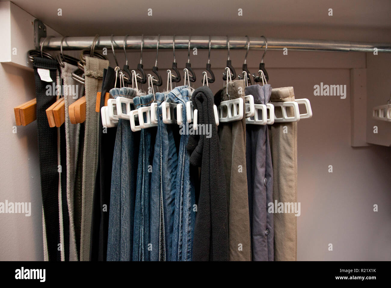 Paia di jeans e pantaloni appesi su grucce appendiabiti in una fila nell' armadio, ben organizzata Foto stock - Alamy