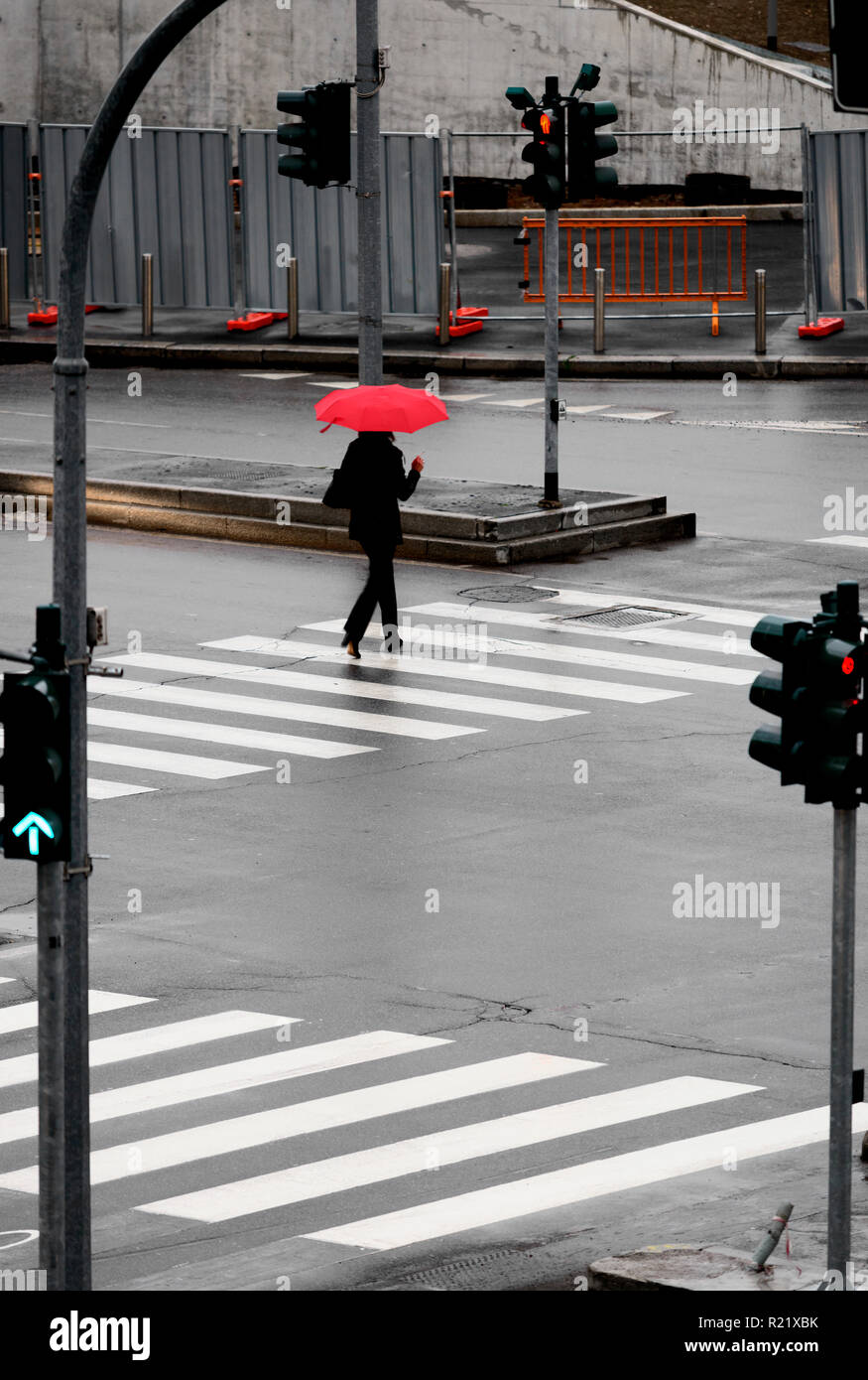 Donna che cammina su crosswalk sotto la pioggia con ombrello rosso Foto Stock