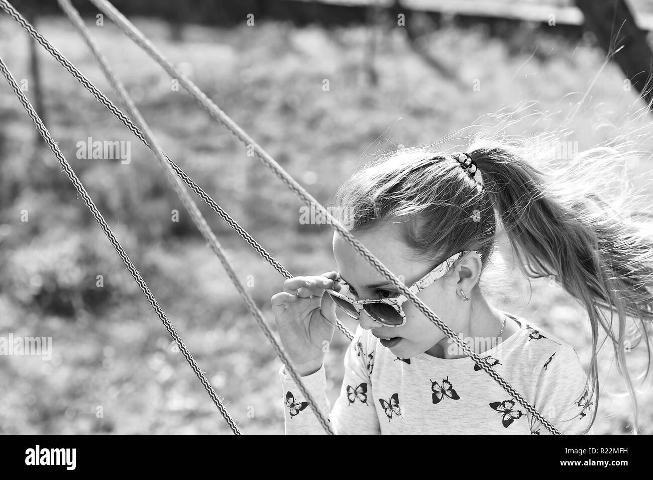 La libertà, lo stile di vita spensierata e divertente. Moda ragazza in occhiali da sole godetevi basculante in giornata di sole. Bambino su altalena in estate cantiere. Bellezza capretto con capelli lunghi sul parco giochi. Infanzia felice concetto. Foto Stock