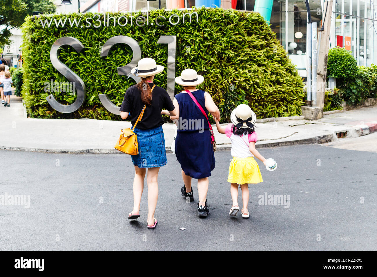 3 generazioni di una famiglia in cappelli attraversando la strada. 2 madri, due figlie e una nipote, Bangkok, Thailandia Foto Stock