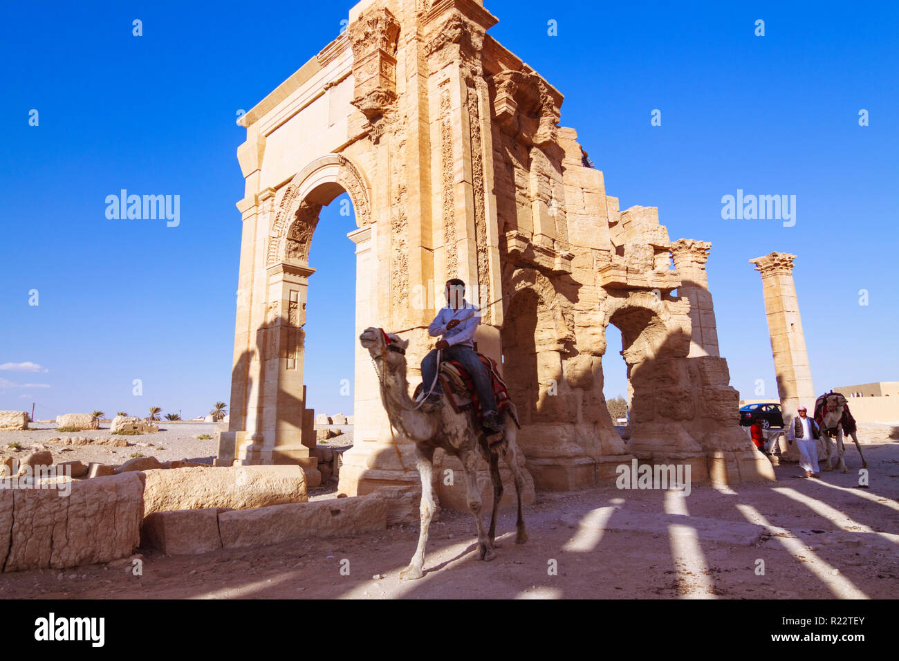 Palmyra, Homs Governatorato, Siria - Maggio 27th, 2009 : un uomo che cavalca un cammello al di sotto del terzo secolo monumentale arco di trionfo di Palmyra, Romano ornamenta Foto Stock