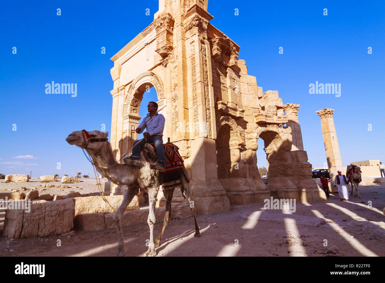 Palmyra, Homs Governatorato, Siria - Maggio 27th, 2009 : un uomo che cavalca un cammello al di sotto del terzo secolo monumentale arco di trionfo di Palmyra, Romano ornamenta Foto Stock