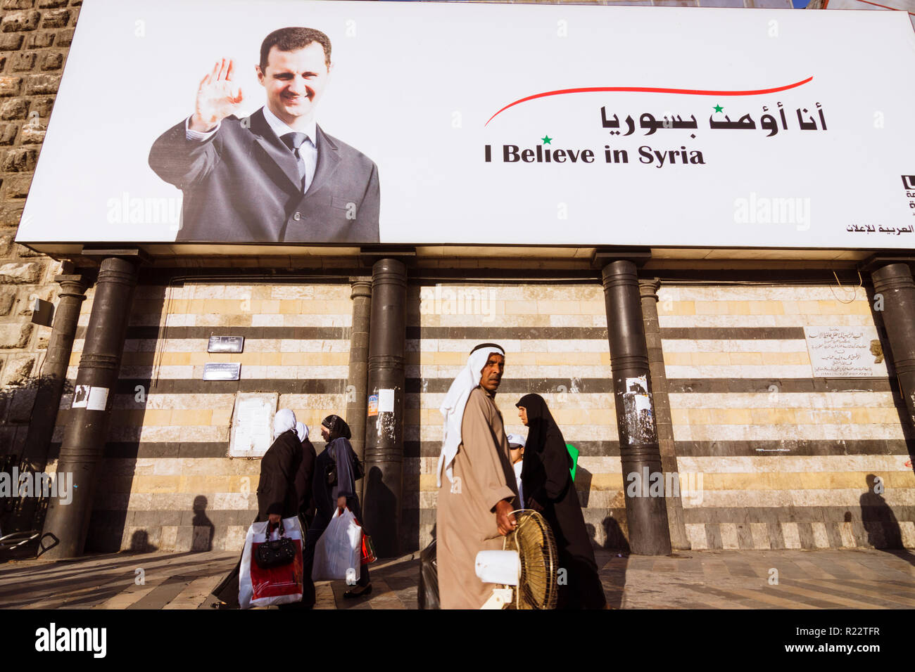 Damasco, Siria : la gente a piedi passato un cartellone del presidente siriano Bashar al-Assad lettura credo in Siria. Foto Stock