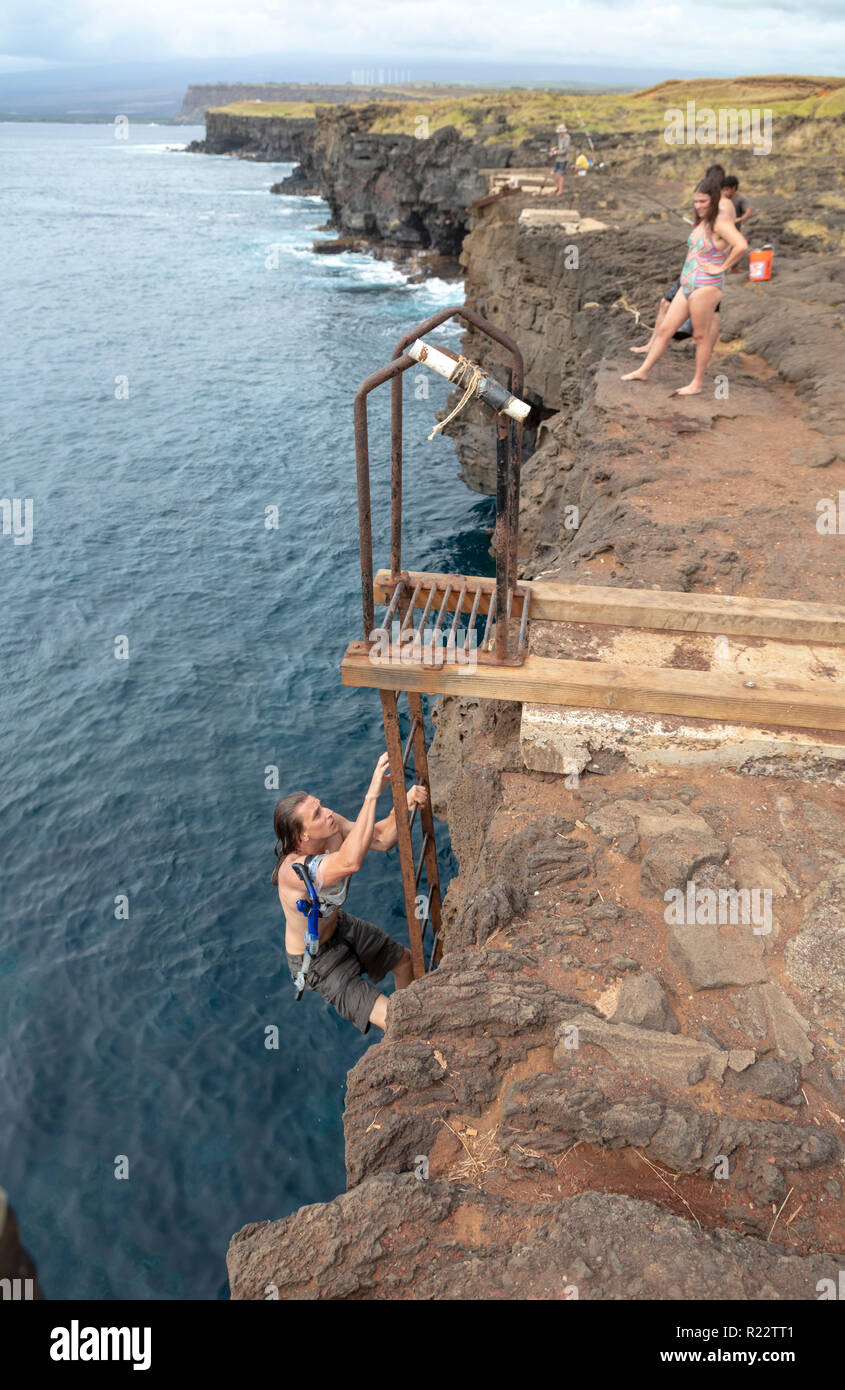 Ka Lae, Hawaii - un giovane uomo si arrampica una scaletta di ruggine su un 40-piede cliff dopo lo snorkeling nell'Oceano Pacifico a sud del punto. Il Sud Point è il souther Foto Stock