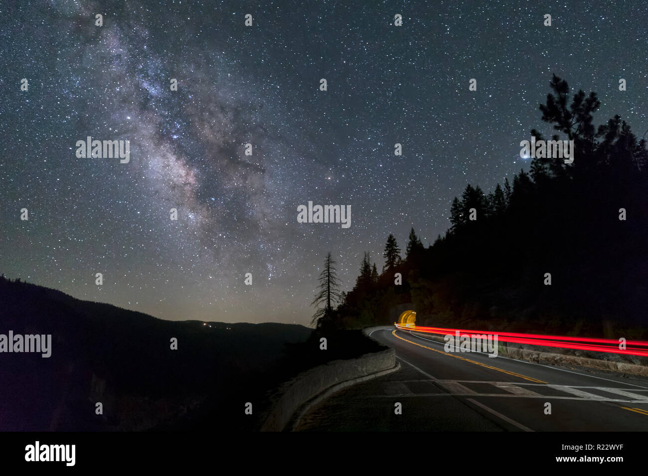 Sotto un cielo notturno con Via Lattea sopra, auto taillights streak attraverso la scena e in un tunnel su grandi botti di strada piana nel Parco Nazionale di Yosemite, CA. Foto Stock