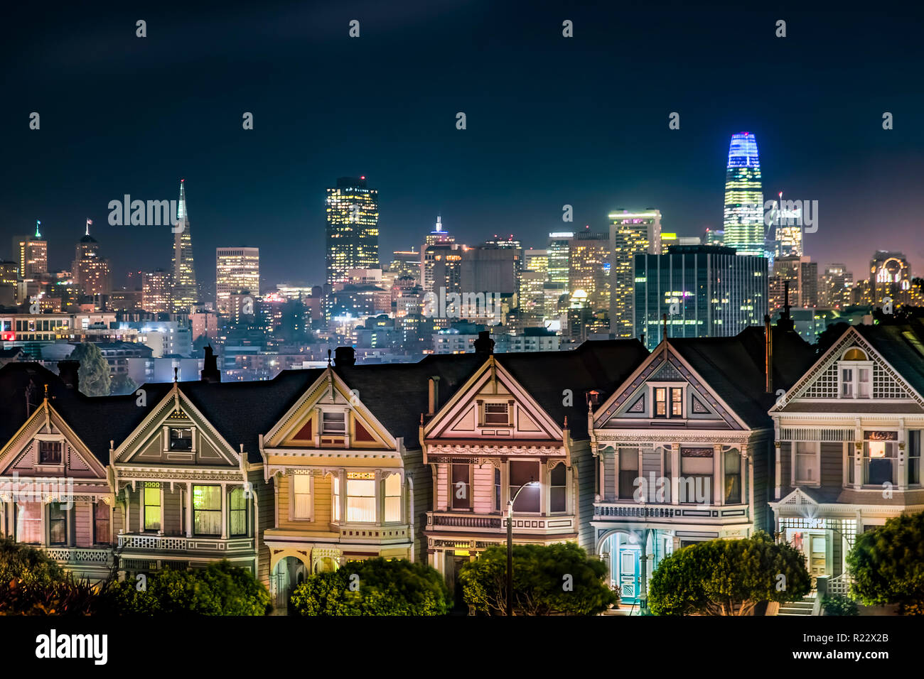 Sostenuto dalla notte skyline della città di San Francisco, in California, l'era vittoriana case vicino Alamo Square Park, sono dipinte in colori di accento Foto Stock