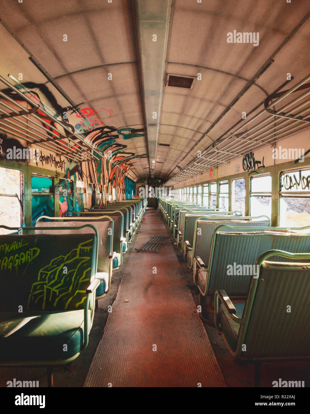 Coperto di graffiti auto treno all'interno. Grungy aspetto di un carrello abbandonato con sedili tagliati e blue graffiti sulle pareti e finestre. Foto Stock