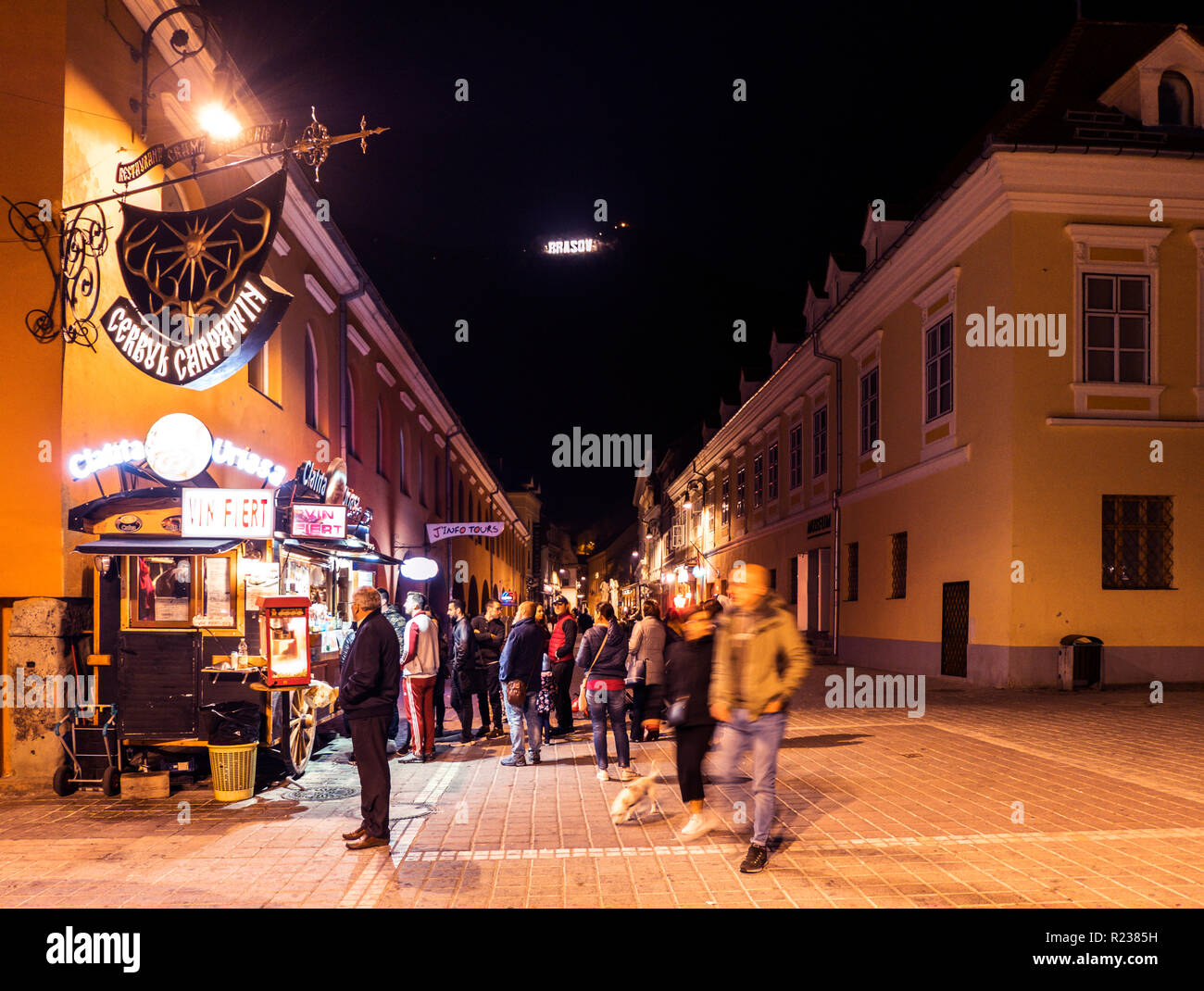 Brasov, Romania - 21 Ottobre 2018: affollata piazza della città vecchia di Brasov di notte, con la città di segno sulla montagna di Tampa illuminato Foto Stock
