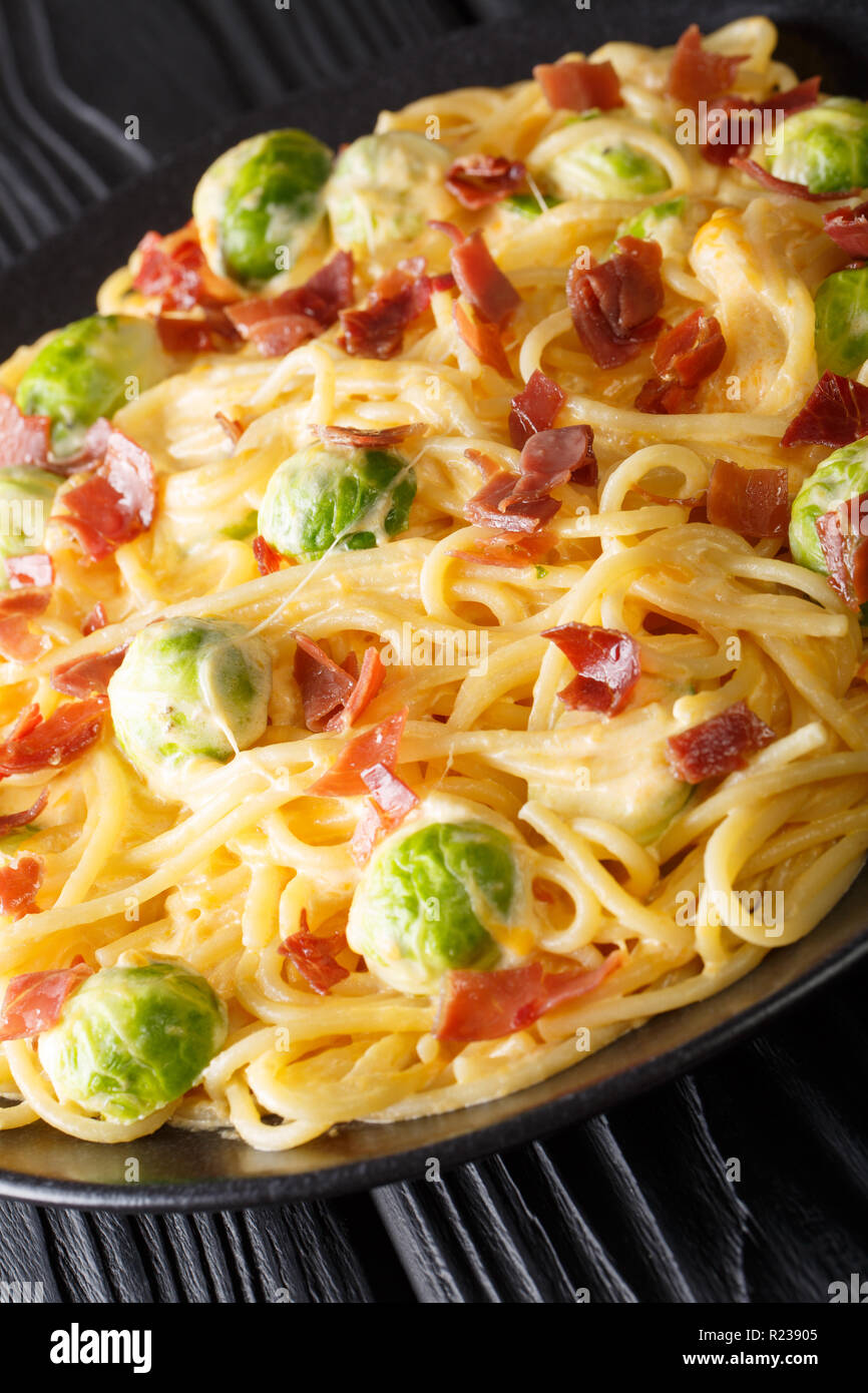 Italian spaghetti con cavoletti di Bruxelles e prosciutto con salsa al formaggio close-up su una piastra sul piano verticale. Foto Stock