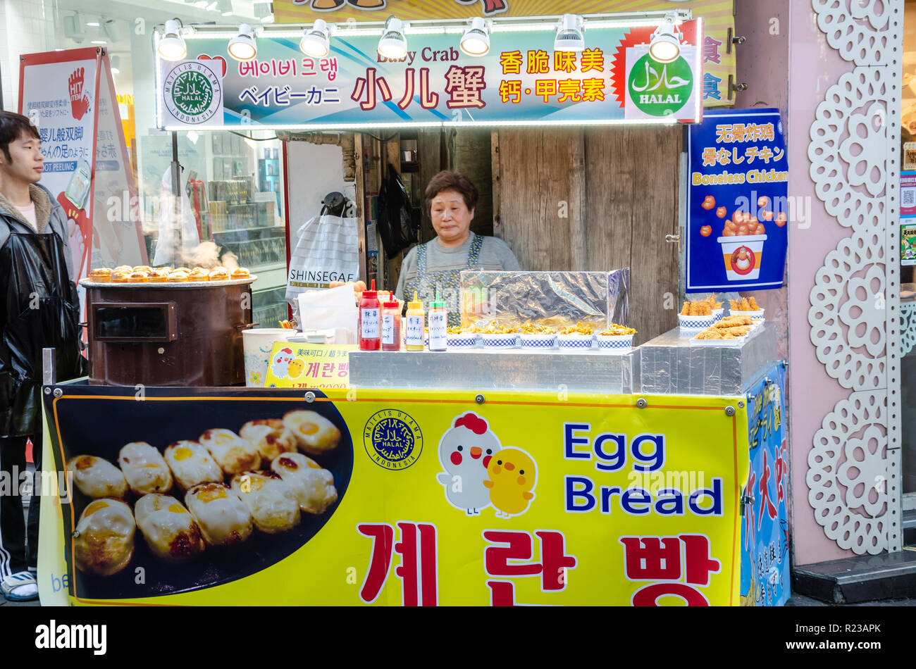 Una signora mans il suo cibo di strada in stallo a Myeongdong a Seul, in Corea del Sud. Foto Stock