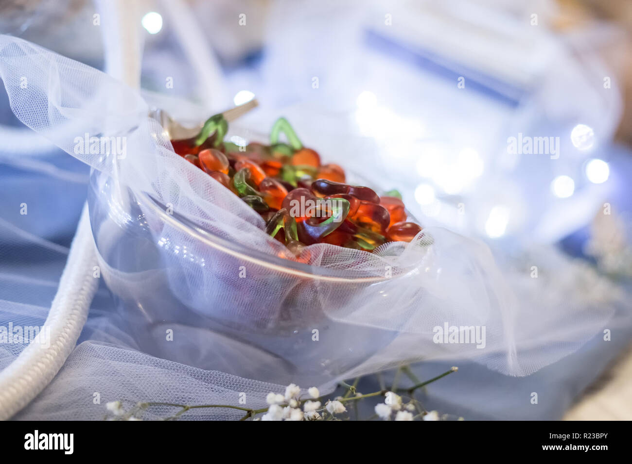 Rosso e verde caramella gommosa sul vasetto in vetro, decorazione per cerimonia sul tavolo blu con corda e vaso illuminato Foto Stock