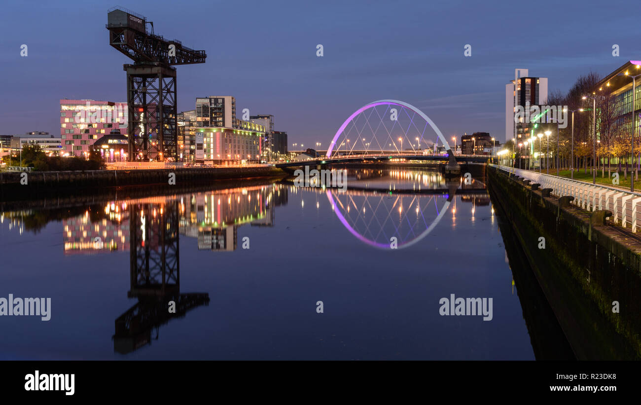 Glasgow, Scotland, Regno Unito - 4 Novembre 2018: Il moderno Clyde Arc bridge è illuminata di notte attraverso il fiume Clyde accanto all'iconico Finnieston gru in Gla Foto Stock