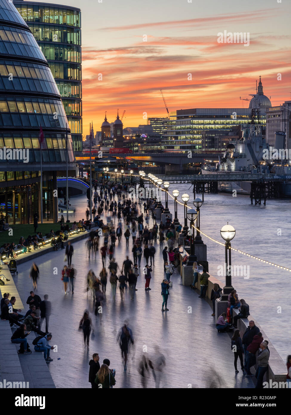 London, England, Regno Unito - 27 Settembre 2018: pedoni e turisti a piedi lungo il fiume Thames Path accanto al Municipio e HMS Belfast al tramonto. Foto Stock