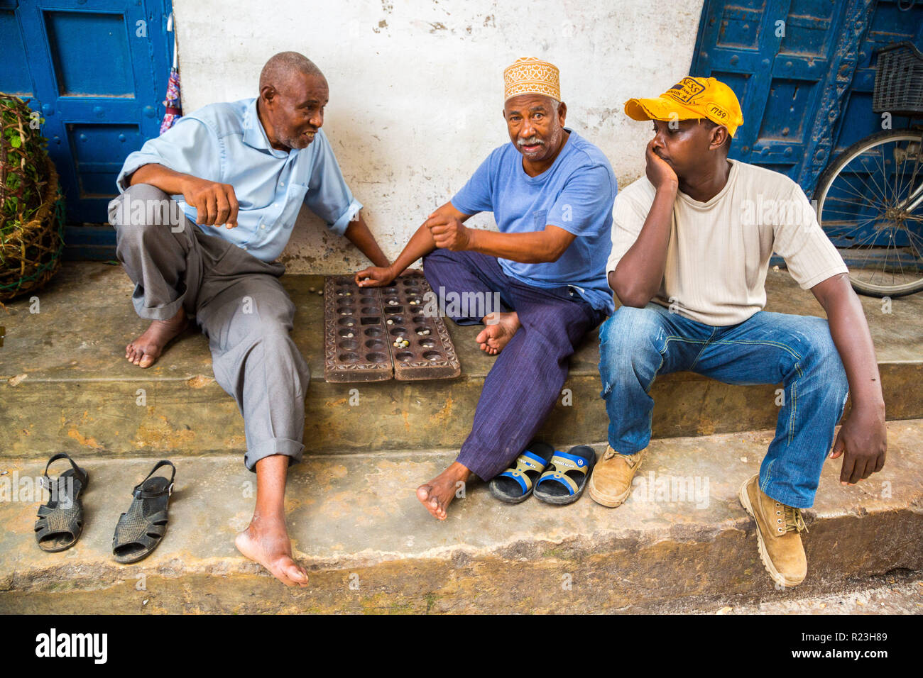 Tre locali africane uomini giocano pensione tradizionale gioco mancala. Stone Town, vecchio centro coloniale della città di Zanzibar, isola di Unguja, Tanzania. Foto Stock