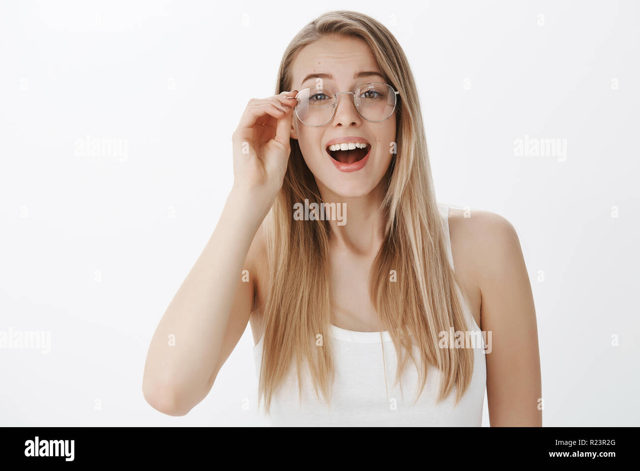 Ragazza mettendo su vetri di essere rimasto sorpreso e felice di vedere volto familiare nella massa, sospiri sollevato e stupiti toccando di RIM di eyewear rendendo impressionato Foto Stock