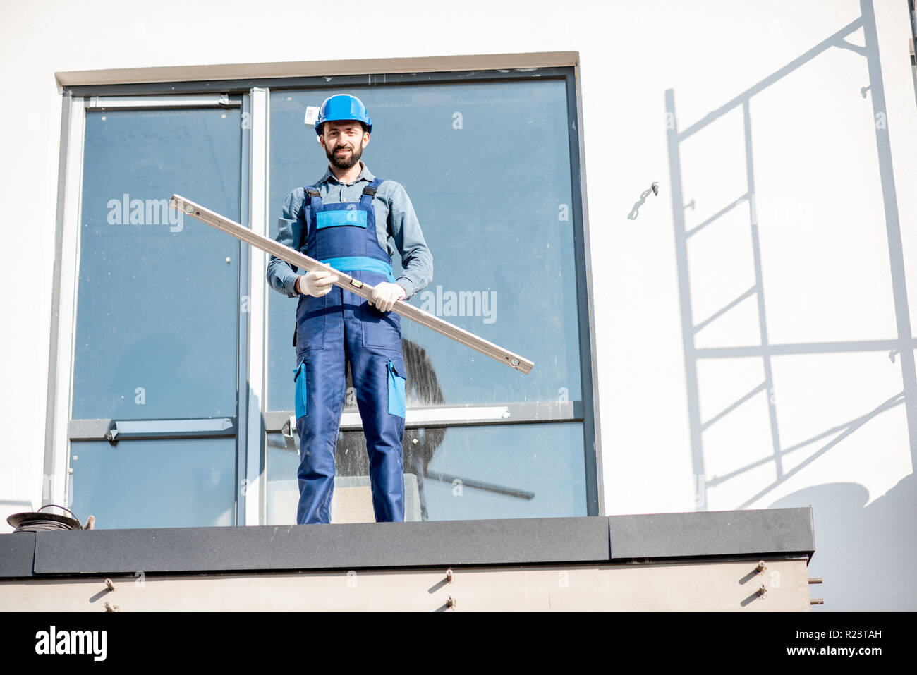 Portraiit di un costruttore in uniforme in piedi con il livello sul balcone di una casa nuova sul sito in costruzione Foto Stock