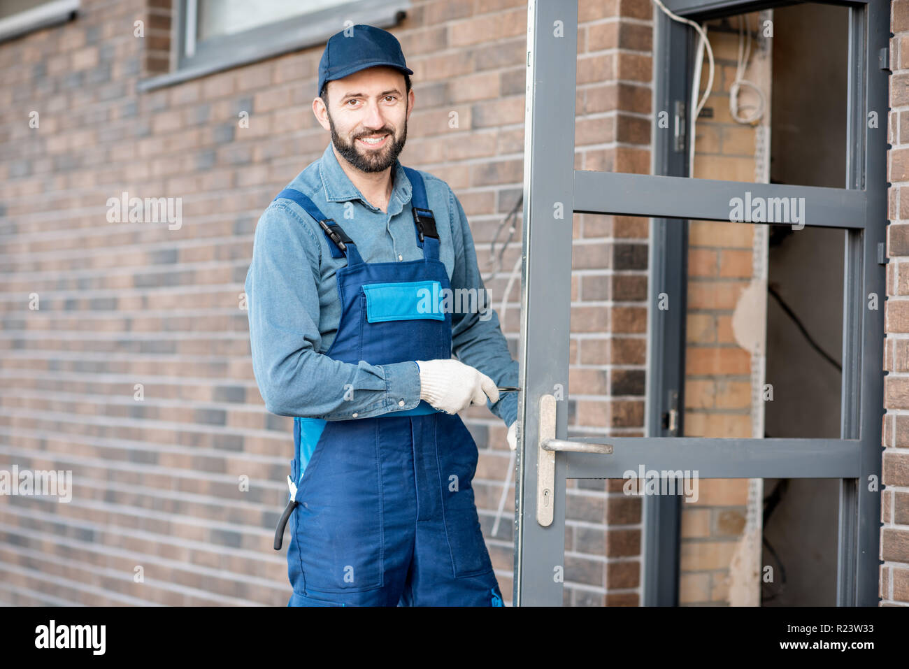 Builder in uniforme di installare la serratura di una porta nella porta di ingresso di una nuova casa all'aperto Foto Stock