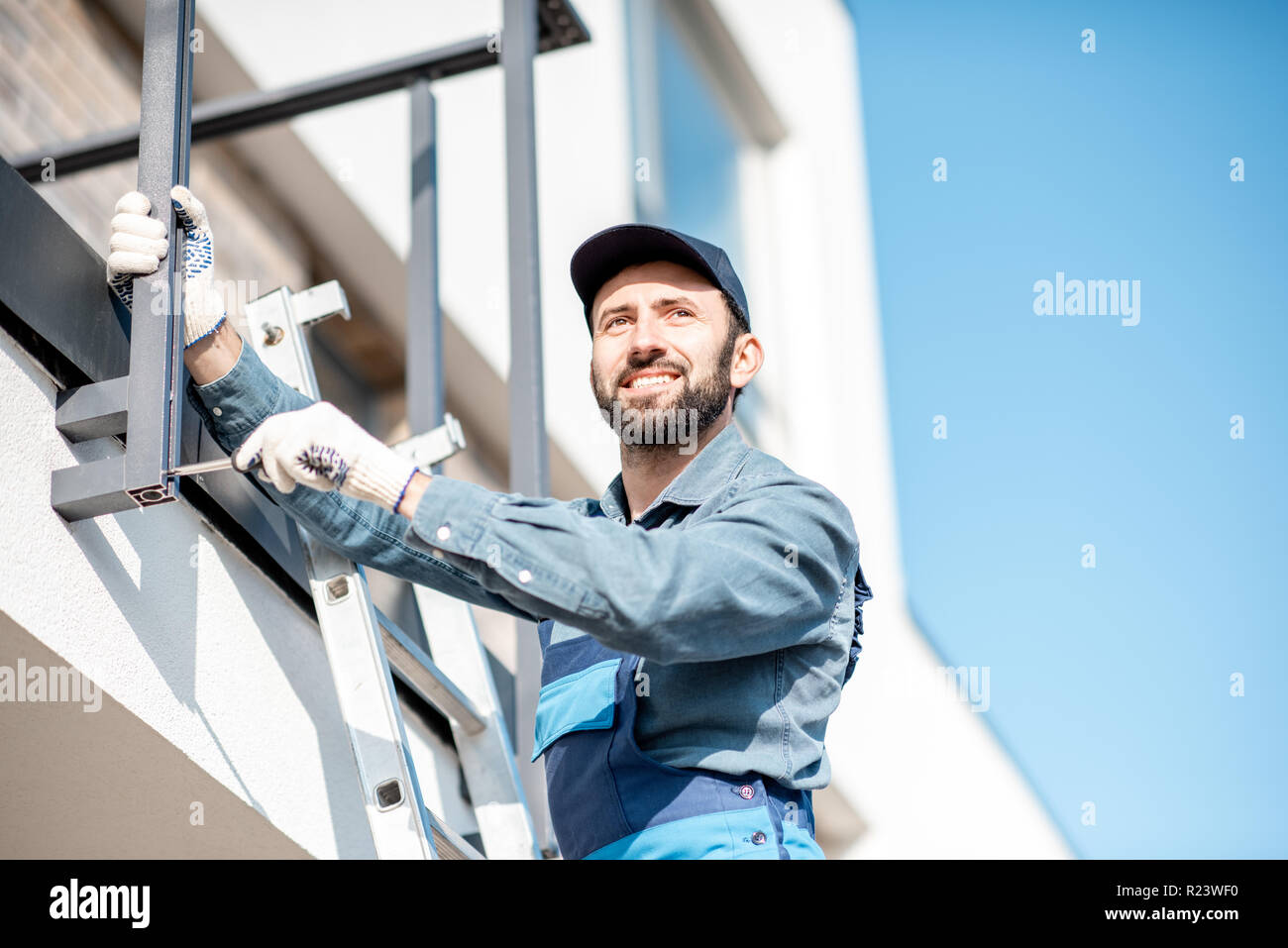 Builder in uniforme blu montaggio recinzione in alluminio sul balcone del nuovo edificio Foto Stock