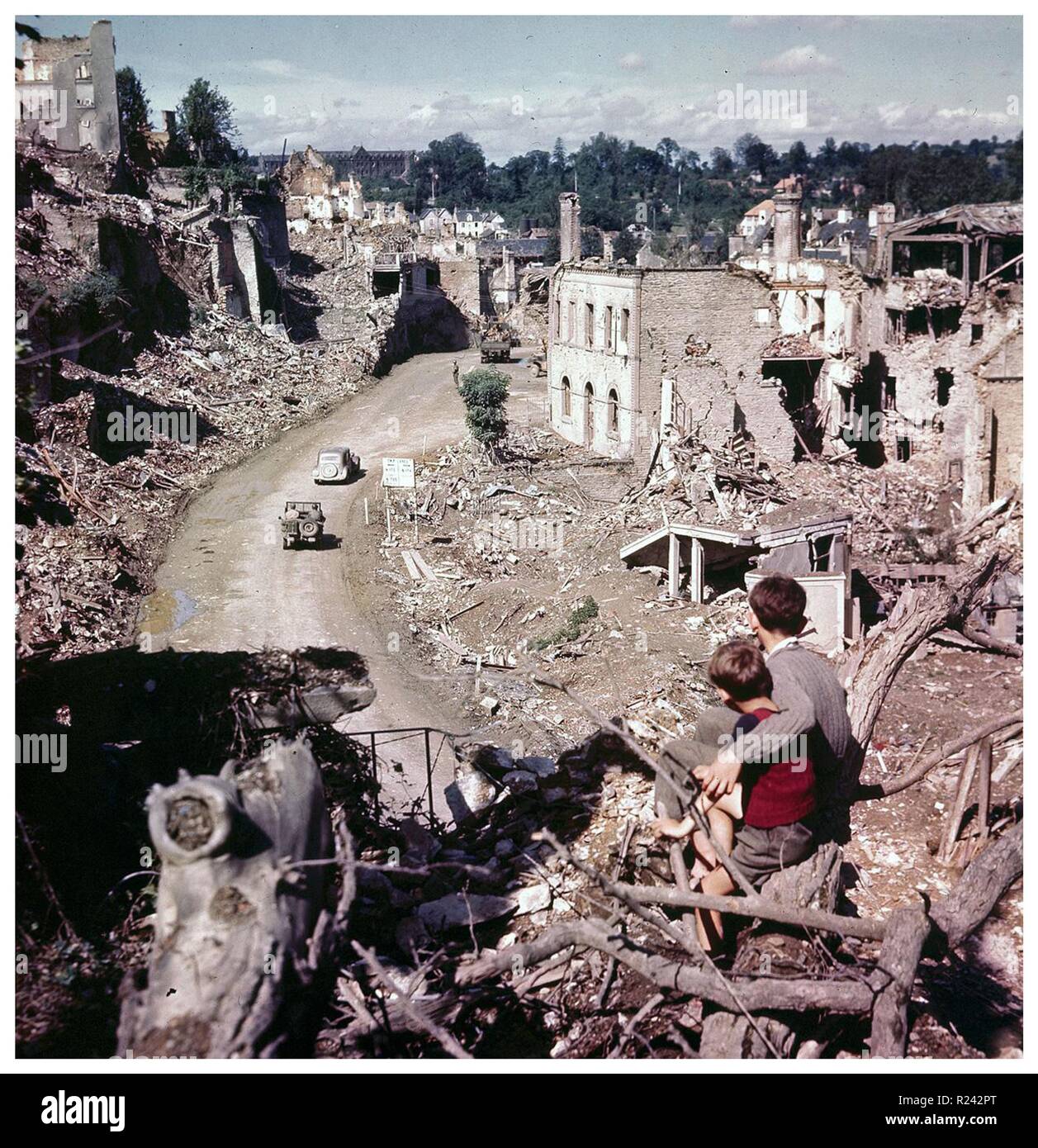 Ragazzi francese sedersi e osservare alcuni veicoli alleati passando attraverso il francese guerra mondiale due danneggiato città di Saint-LA', 1944 Foto Stock