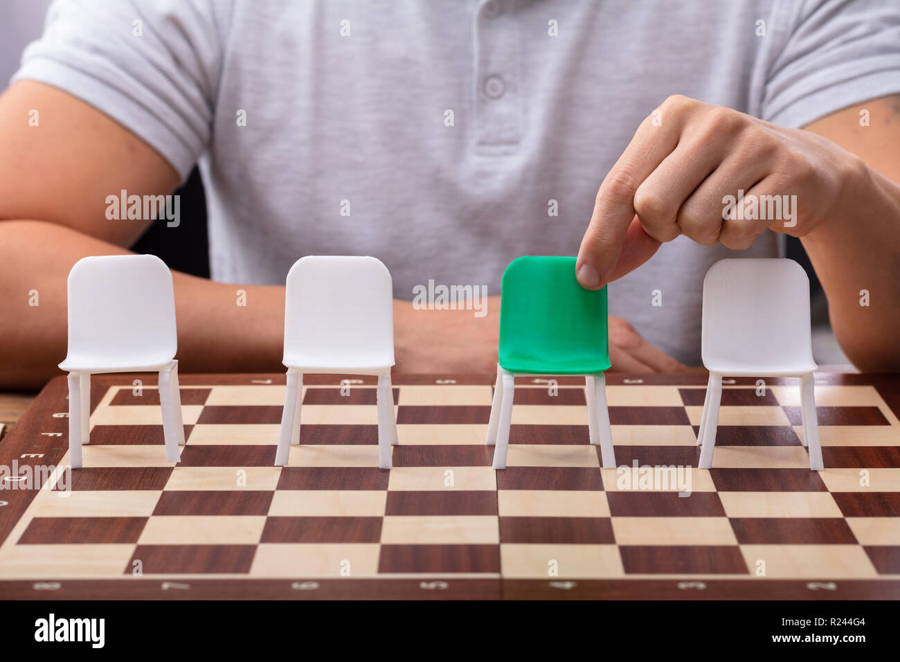 Mano d'uomo scegliendo sedia verde tra gli altri sulla scacchiera Foto Stock