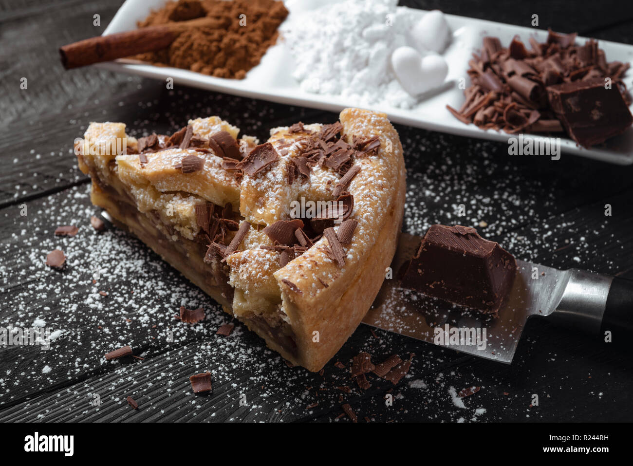 Fetta di torta di mele con zucchero a velo e il cioccolato, su un coltello su un nero tavolo rustico e una piastra con cannella.pasticceria. Dolci da forno. Foto Stock