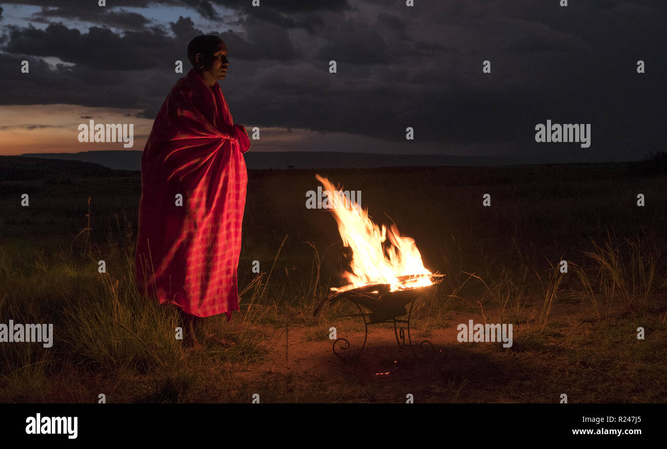 Masai Mara uomo indossando il tradizionale rosso tribale coperta dal campo di fuoco, il Masai Mara National Park, Kenya, Africa orientale, Africa Foto Stock