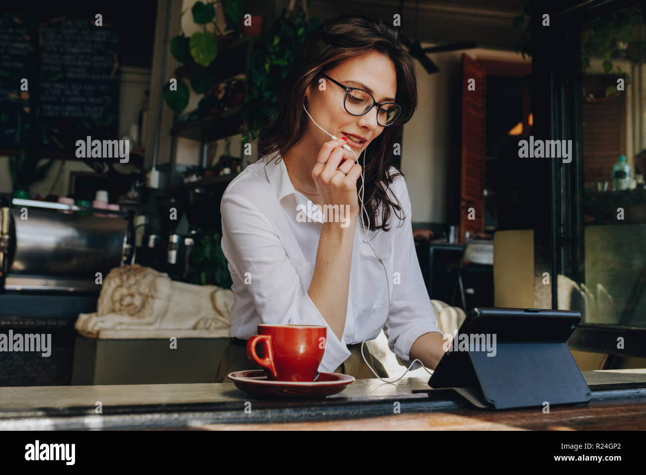 donna d'affari che sta facendo una video chat su un tablet digitale mentre è seduta al bar. Donna seduta al tavolo della finestra al bar e videochiamata usando e. Foto Stock