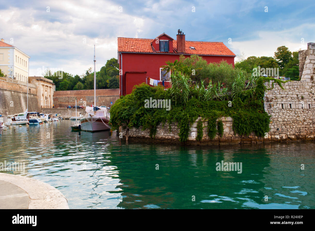 Accogliente pittoresca città di Zadar, Croazia. Red House tra le verdi foglie d'edera nei pressi di acqua color smeraldo dove barche e yacht sono flottanti. Drammatica nuvoloso mor Foto Stock