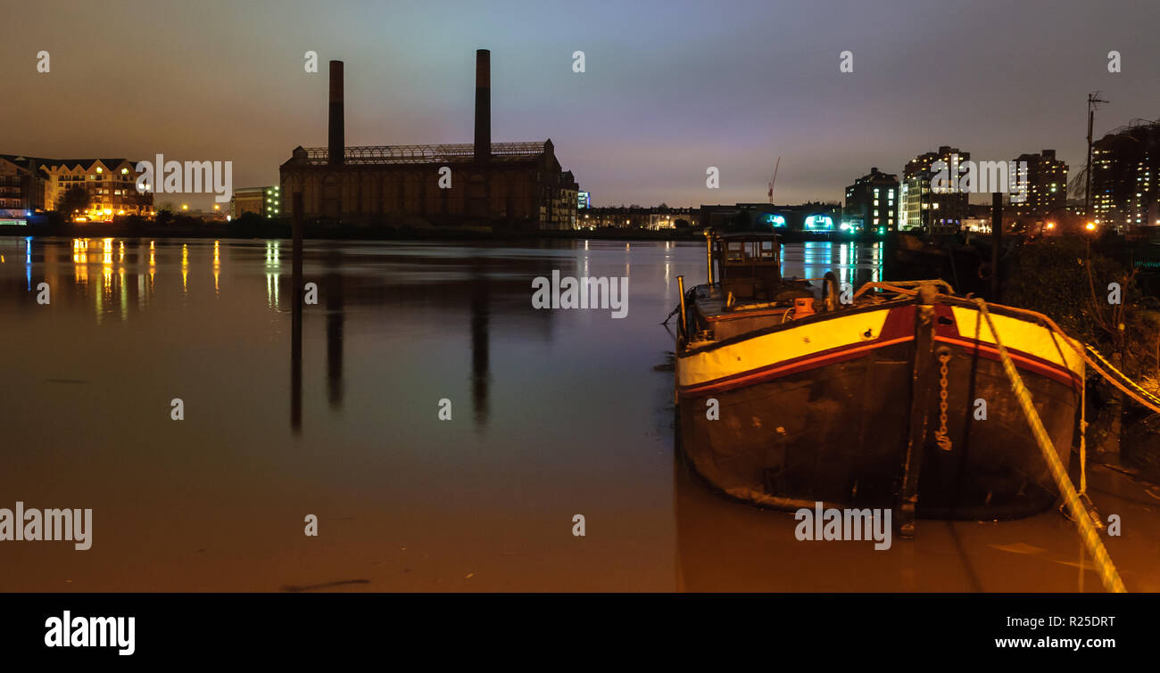 London, England, Regno Unito - 2 Gennaio 2013: una casa galleggiante è ancorato al fiume Tamigi a Battersea di notte, con le partite su strada della stazione di potenza sul Chelse Foto Stock