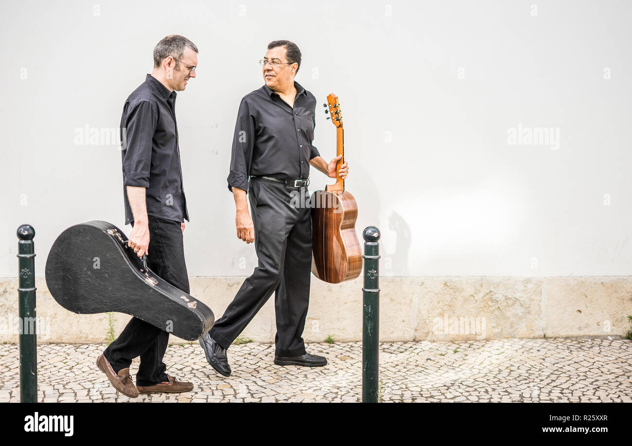 Due chitarristi a piedi con i loro strumenti sulla pavimentazione mediante la parete bianca, Alfama, Lisbona, Portogallo Foto Stock