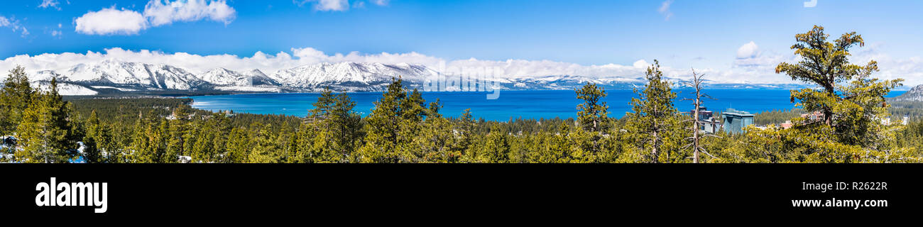 Vista panoramica verso il lago Tahoe su una soleggiata giornata chiara; montagne della Sierra coperte di neve in background; foreste sempreverdi in primo piano Foto Stock