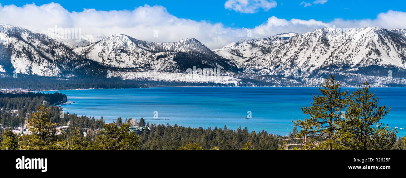 Vista panoramica verso il lago Tahoe su una soleggiata giornata chiara; montagne della Sierra coperte di neve in background; foreste sempreverdi in primo piano Foto Stock