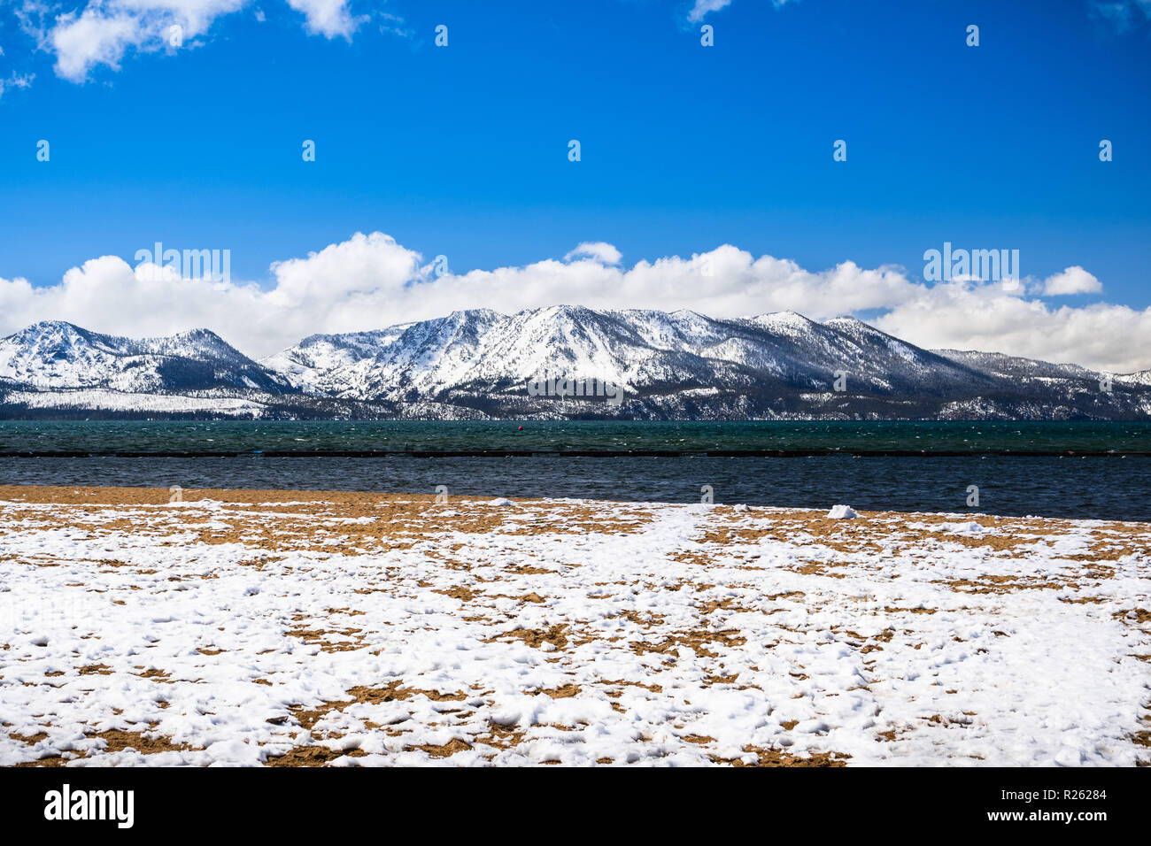 South Lake Tahoe coperta di neve spiaggia di sabbia in una giornata di sole; montagne della Sierra coperte di neve in background; California Foto Stock