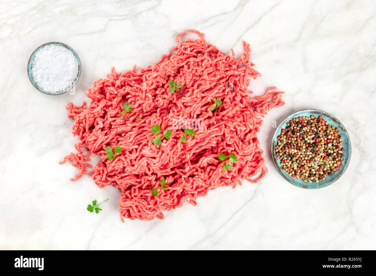 Una foto aerea di carni macinate con sale, pepe e prezzemolo, girato dalla parte superiore su un marmo bianco lo sfondo con un posto per il testo Foto Stock